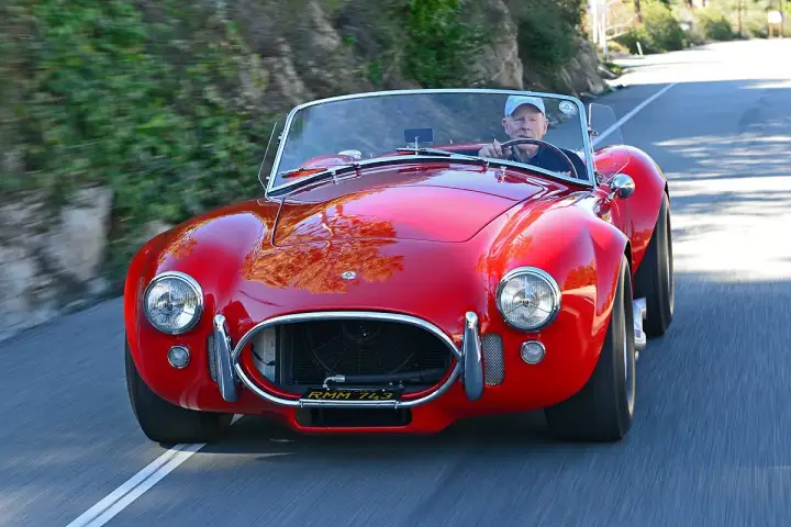 Ein Mann fährt einen roten Shelby Cobra 427 auf einer kurvigen Straße.